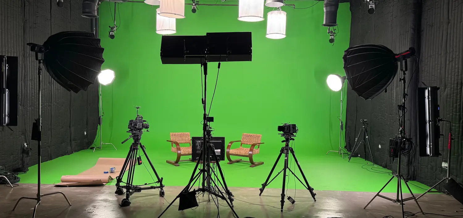 On location: a green screen cyclorama lit with large softboxes and an overhead space-light grid, two chairs and three cameras set for an interview
