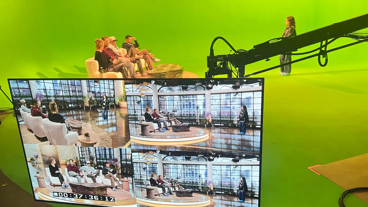 On-location build: a green screen cyclorama with a jib arm over a seated panel, and a monitor showing the finished composited environment